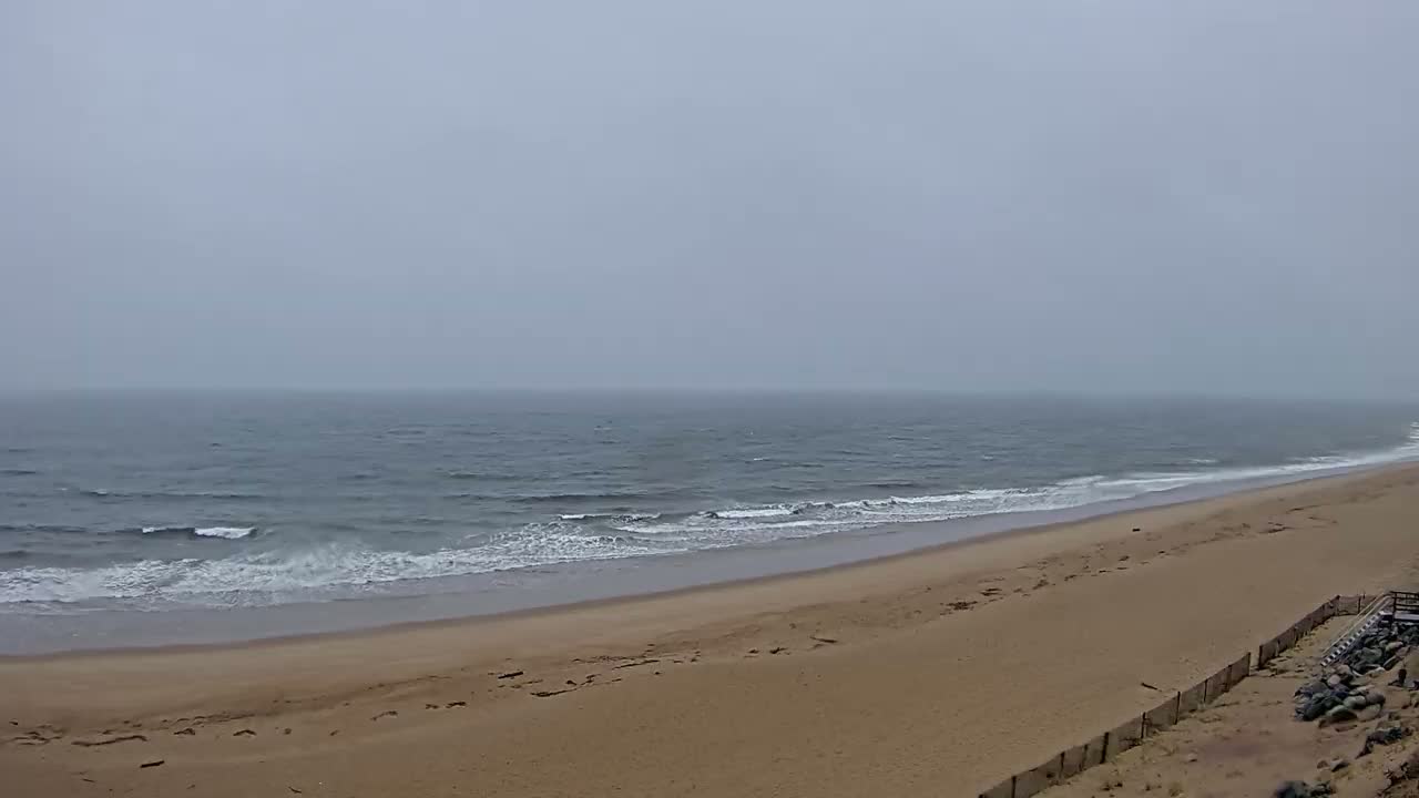 A sandy beach slopes down to a gray, wavy ocean under a foggy sky.