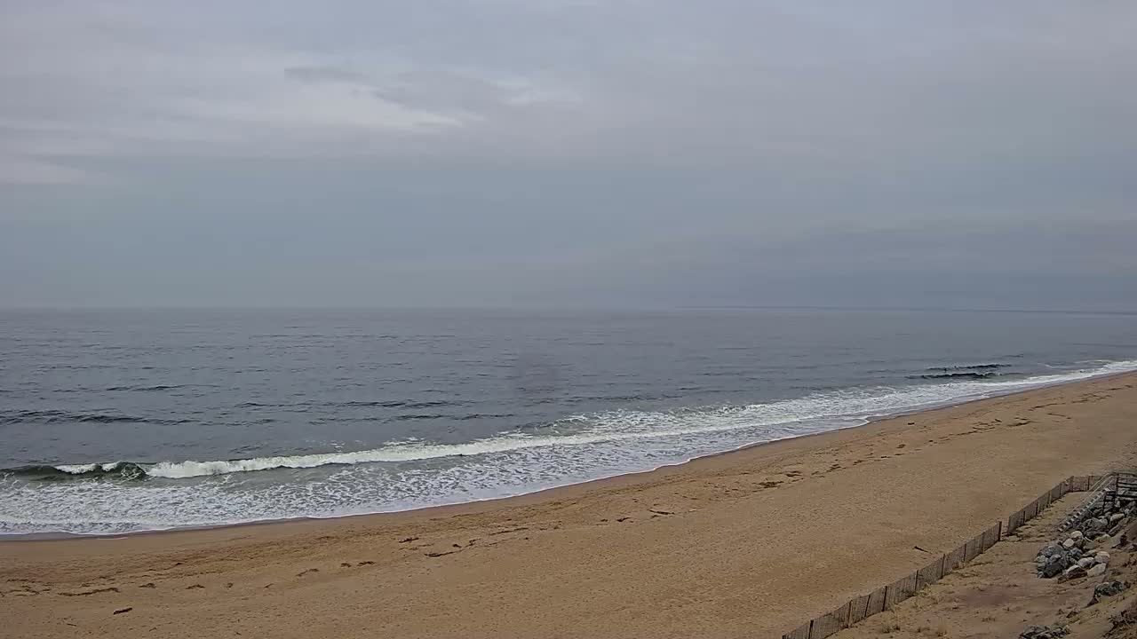 A sandy beach slopes down to a gray ocean with small waves under an overcast sky.