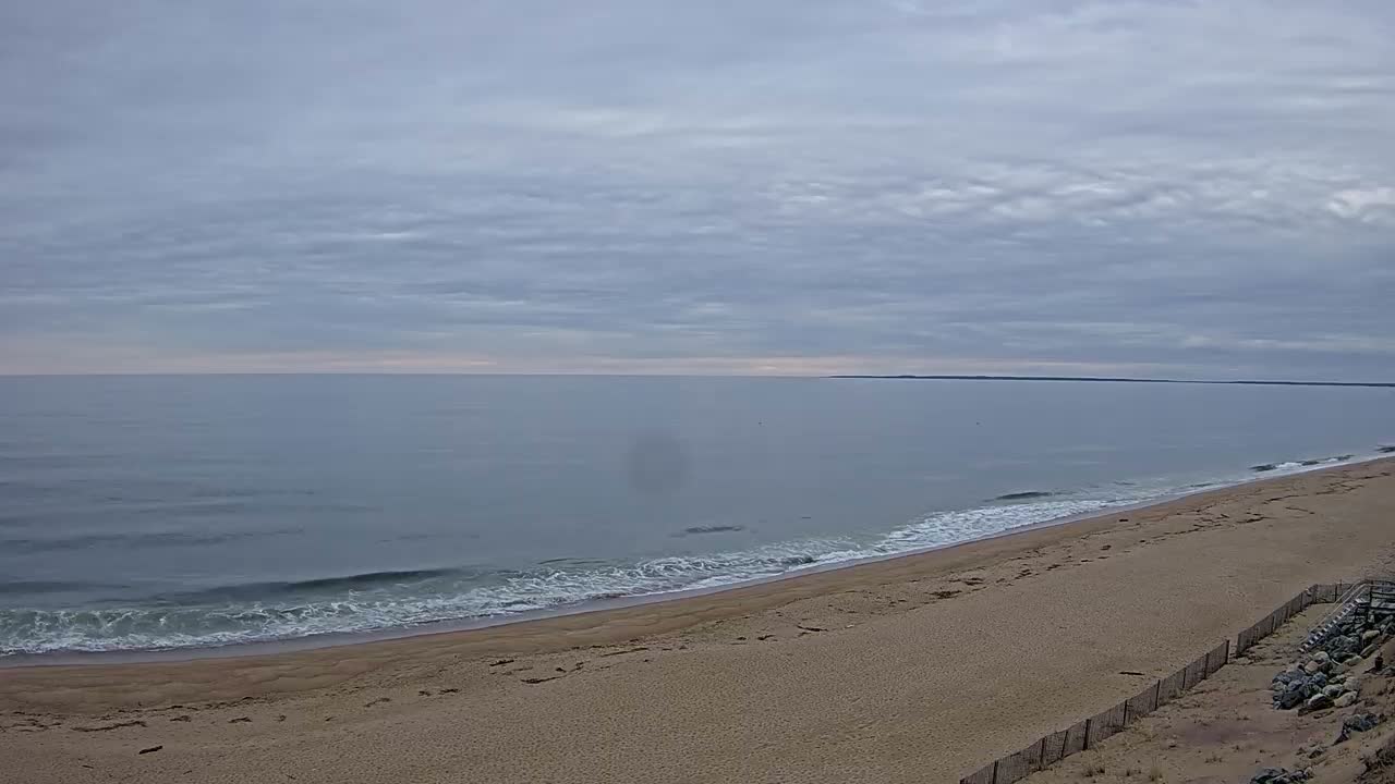 A sandy beach slopes gently down to a calm ocean under a mostly cloudy sky.
