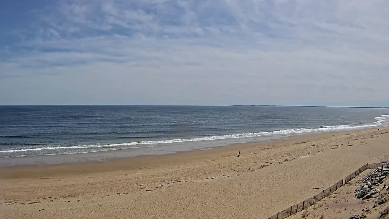 A wide sandy beach stretches to a calm ocean under a partly cloudy sky.