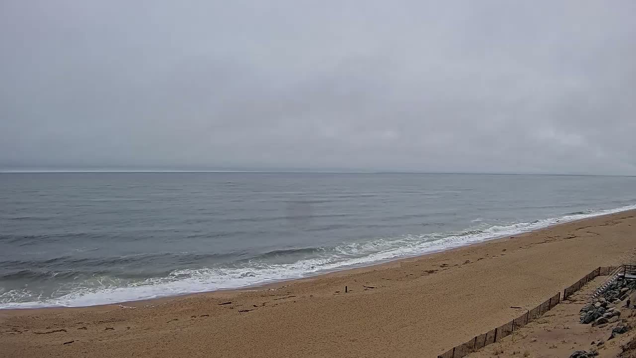 A sandy beach slopes down to a gray, wavy ocean under an overcast sky.