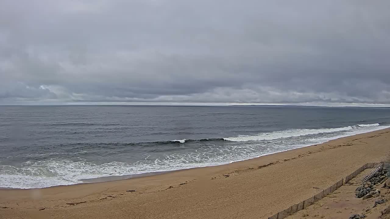 A sandy beach slopes down to a gray ocean with small waves under an overcast sky.