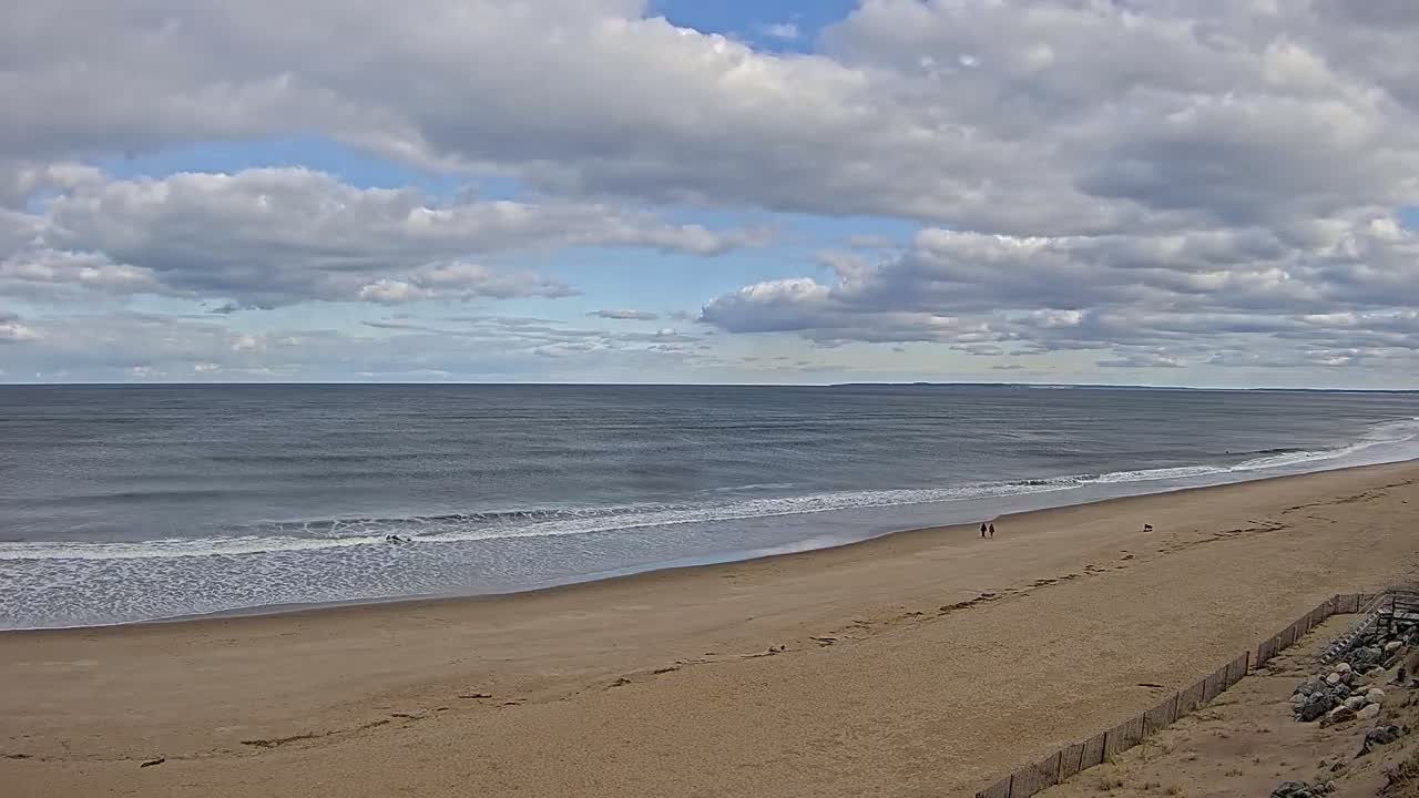 A wide sandy beach stretches to a calm, grey ocean under a partly cloudy sky.