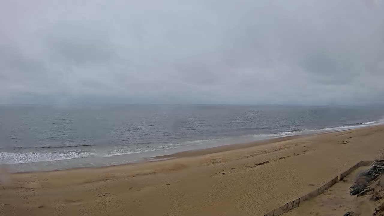 A sandy beach slopes down to a gray, wavy ocean under an overcast sky.