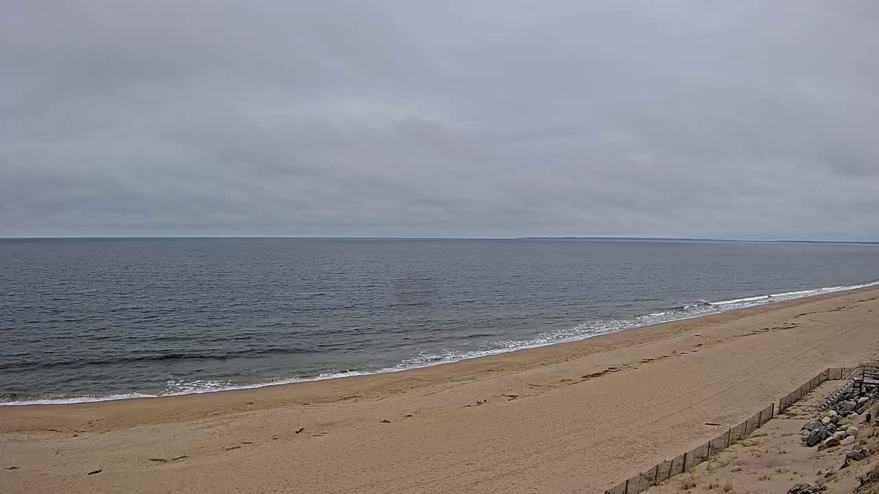 A sandy beach slopes down to a calm, grey ocean under an overcast sky.