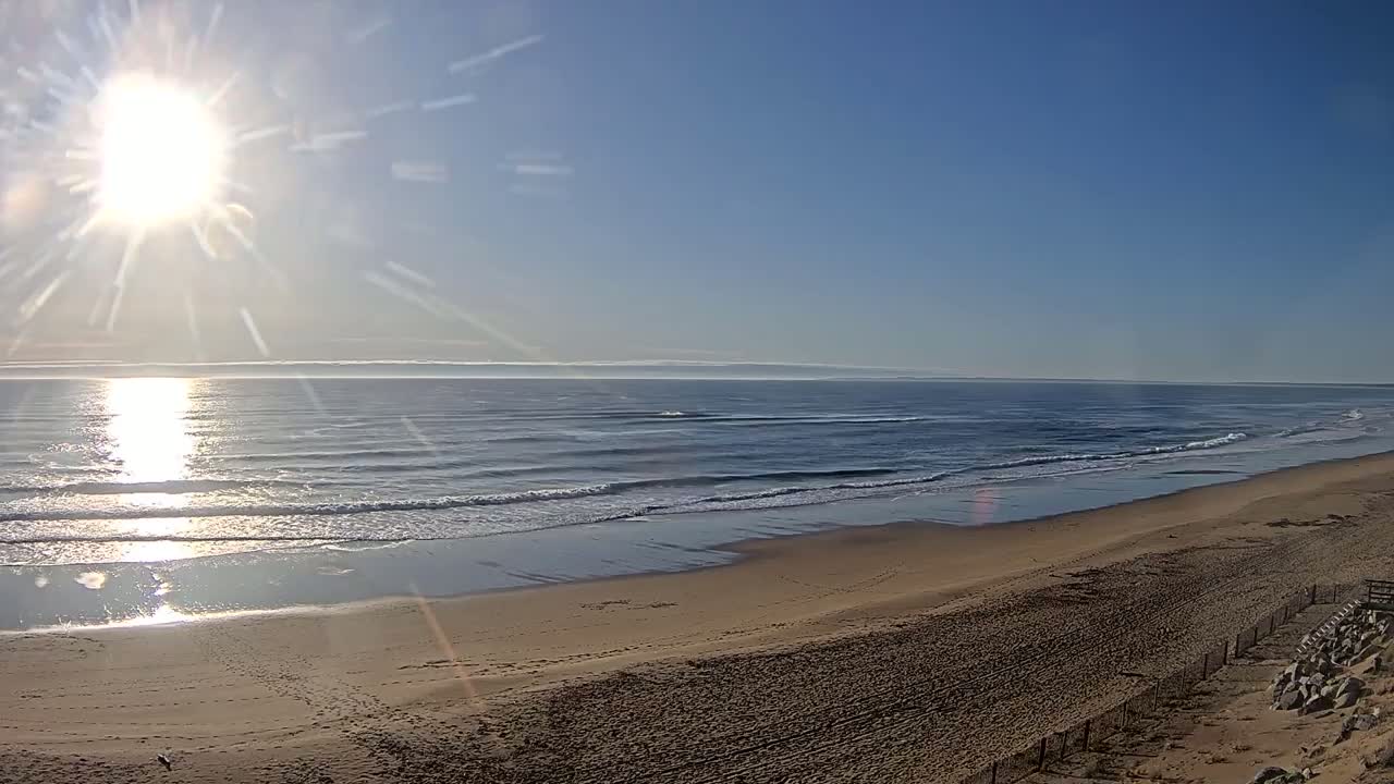 A sandy beach stretches to a calm ocean under a bright, sunny sky.