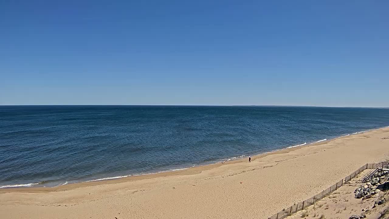 A wide sandy beach stretches along a calm, blue ocean under a clear, blue sky.