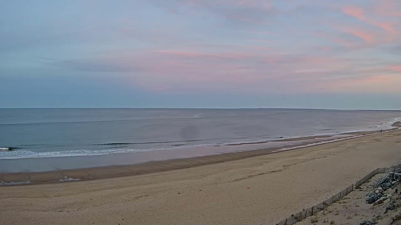 A long, sandy beach slopes gently down to a calm ocean under a pale pink and blue sky.