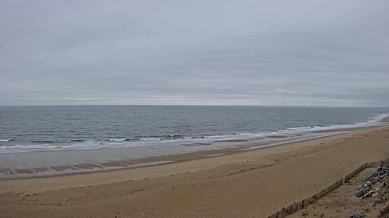 A long sandy beach stretches out to a calm, gray sea under an overcast sky.