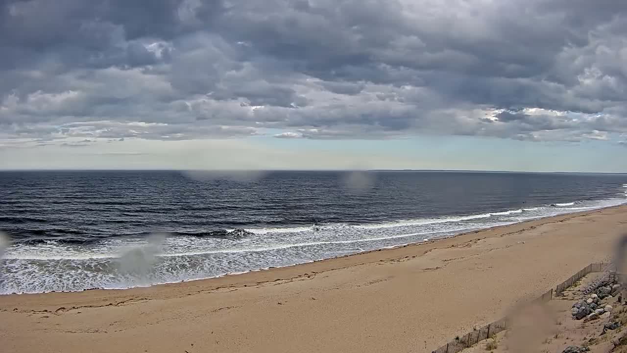 A sandy beach meets a dark ocean with small waves under a cloudy sky.