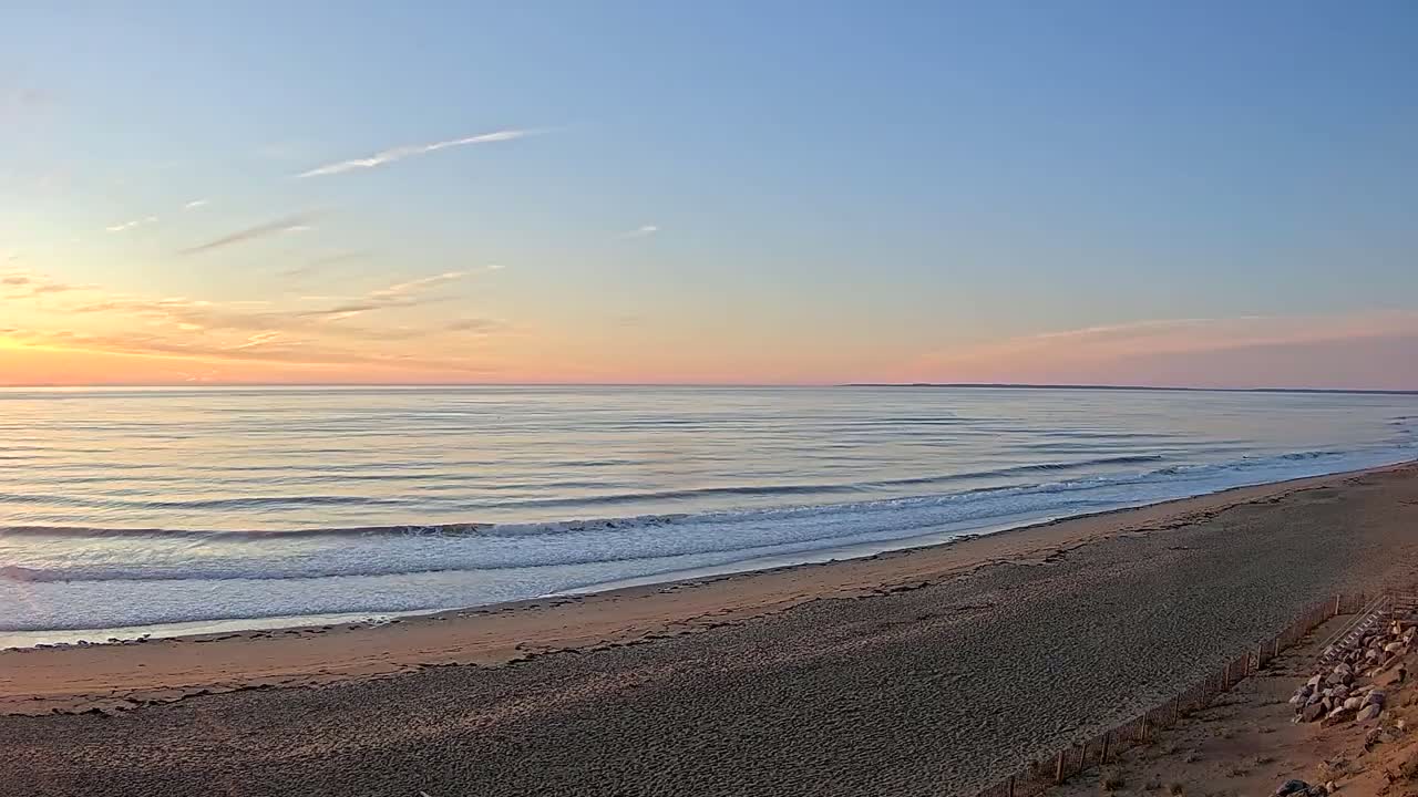 A sandy beach slopes gently down to a calm ocean under a pastel sunset sky.