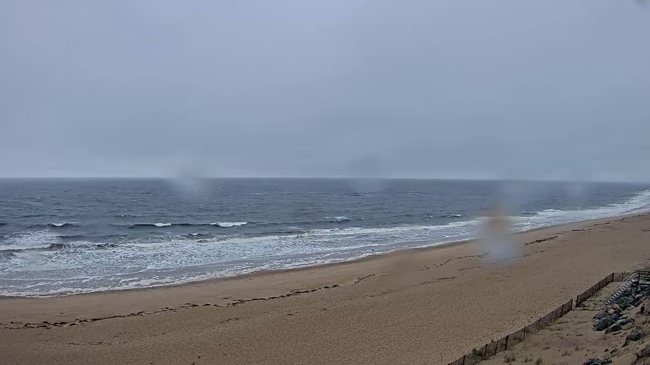 A wide sandy beach slopes down to a dark, wavy ocean under an overcast sky.