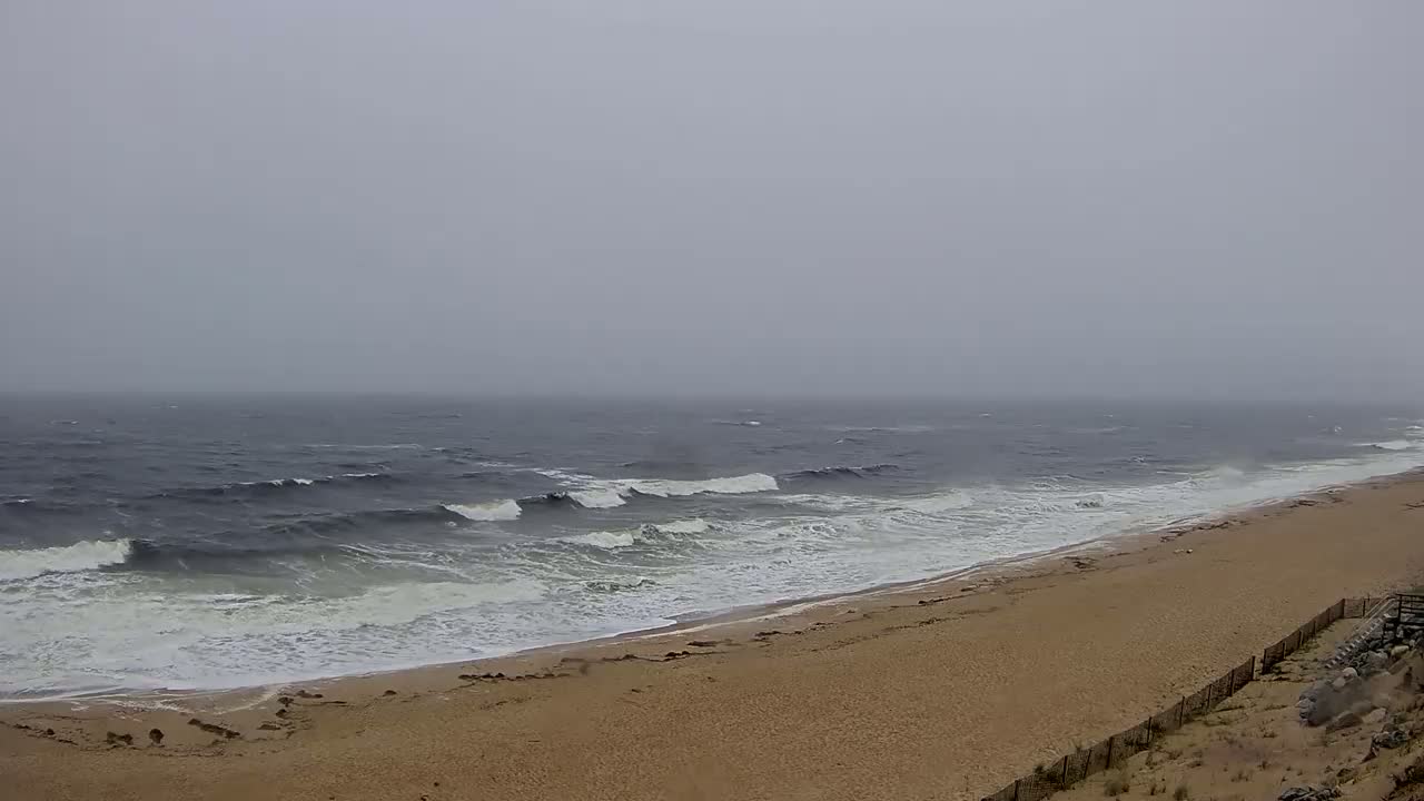 A sandy beach with moderate waves crashes on the shore under a foggy, overcast sky.