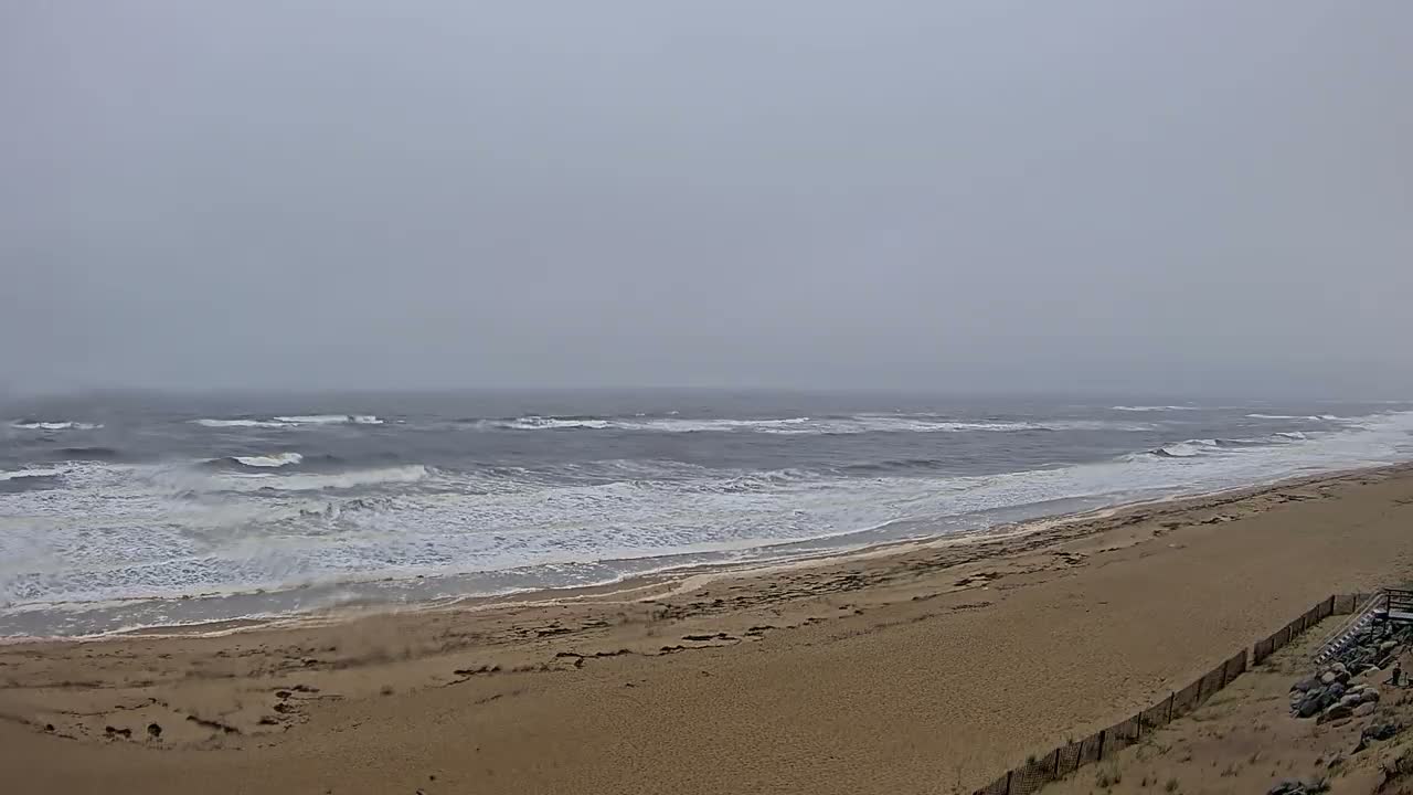 A wide, sandy beach slopes down to a gray, choppy ocean under an overcast sky.