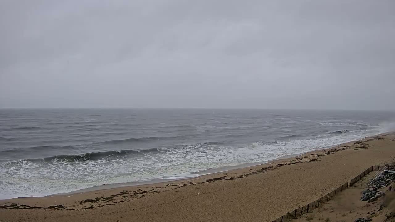 A sandy beach with moderate waves rolling onto the shore under an overcast sky.