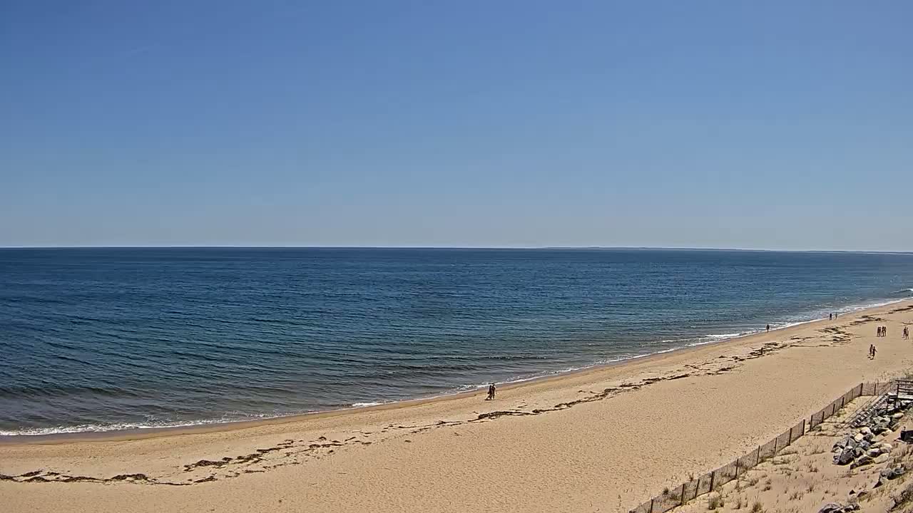 A wide sandy beach slopes down to a calm ocean under a clear blue sky.