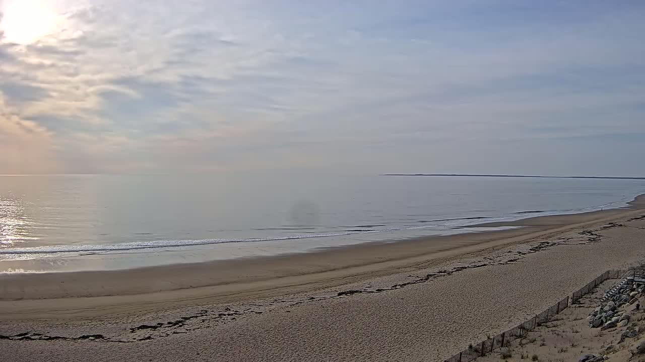 A long, sandy beach stretches out to a calm ocean under a partly cloudy sky.