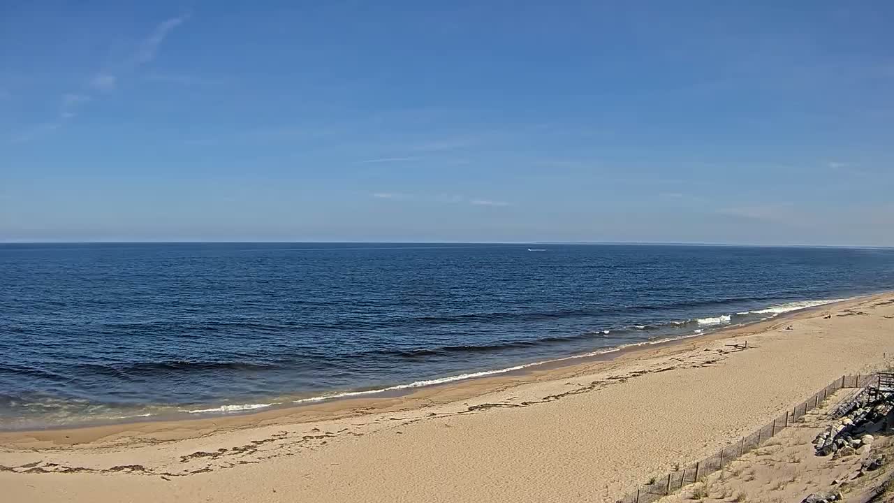 A sandy beach slopes gently down to a calm, dark-blue ocean under a clear, bright blue sky.