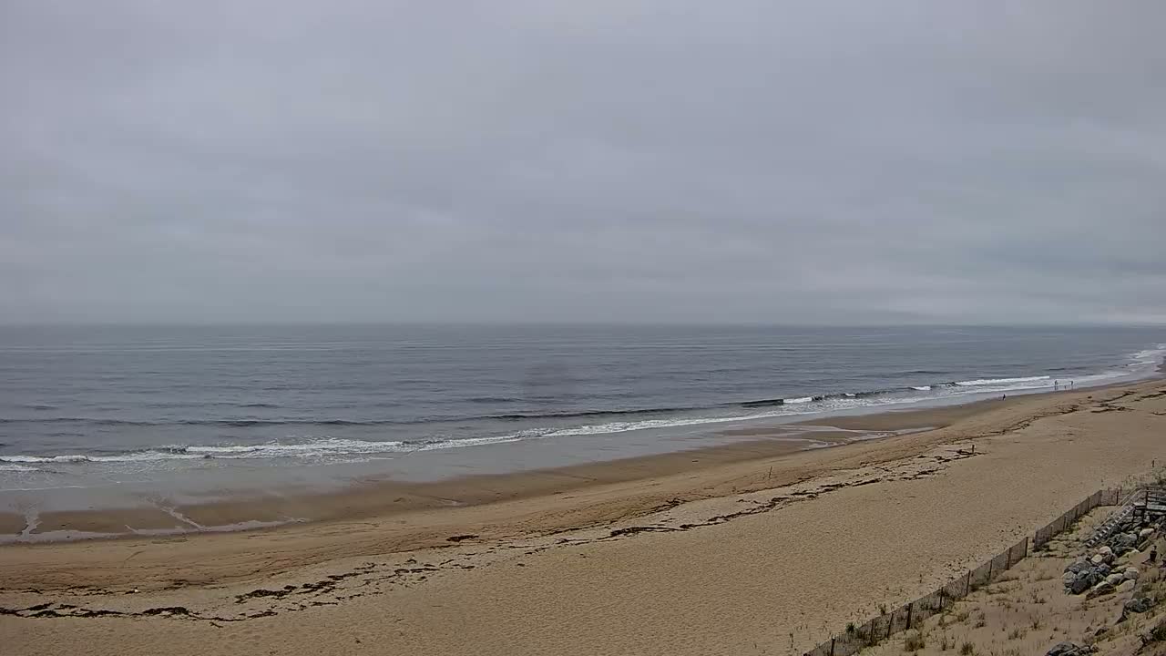 A long sandy beach stretches out to a gray, overcast ocean with small waves.