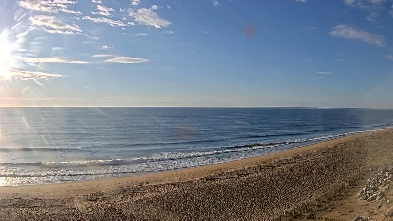 A sandy beach slopes down to a calm ocean under a mostly sunny sky.