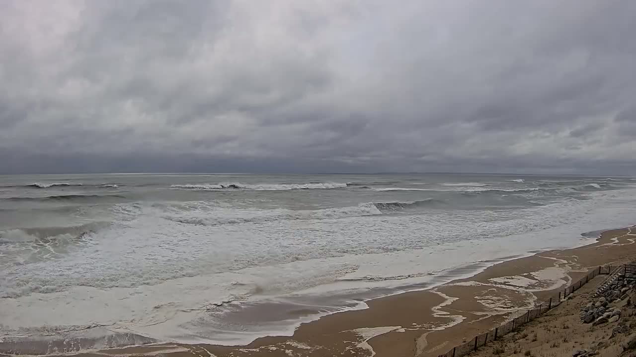 A sandy beach with moderately sized waves crashing on the shore under an overcast sky.