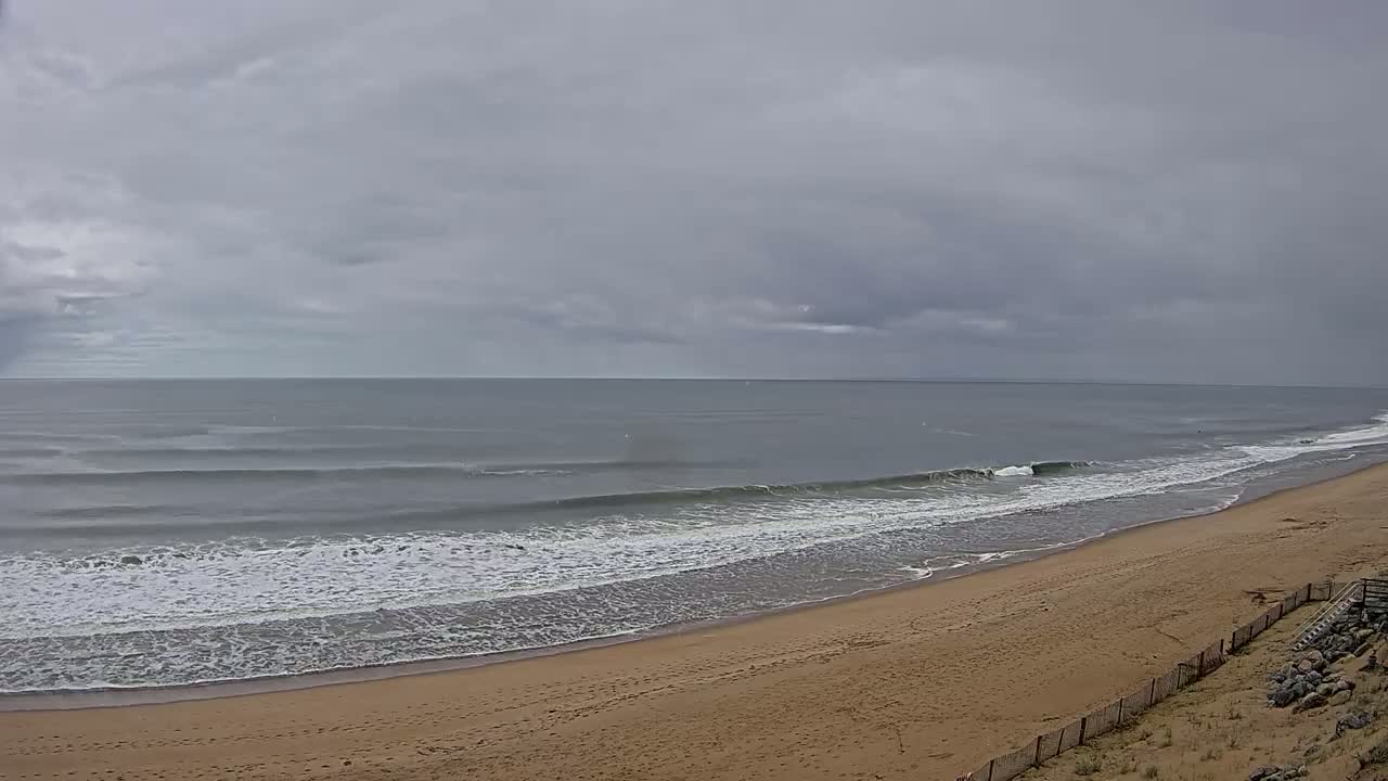 A wide sandy beach slopes down to a grey ocean with small waves under an overcast sky.