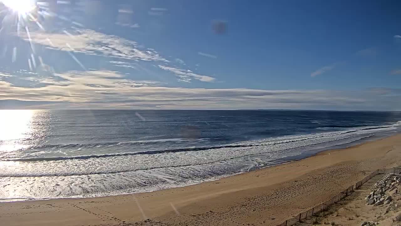 A sandy beach slopes down to a gently rolling ocean under a mostly sunny sky.