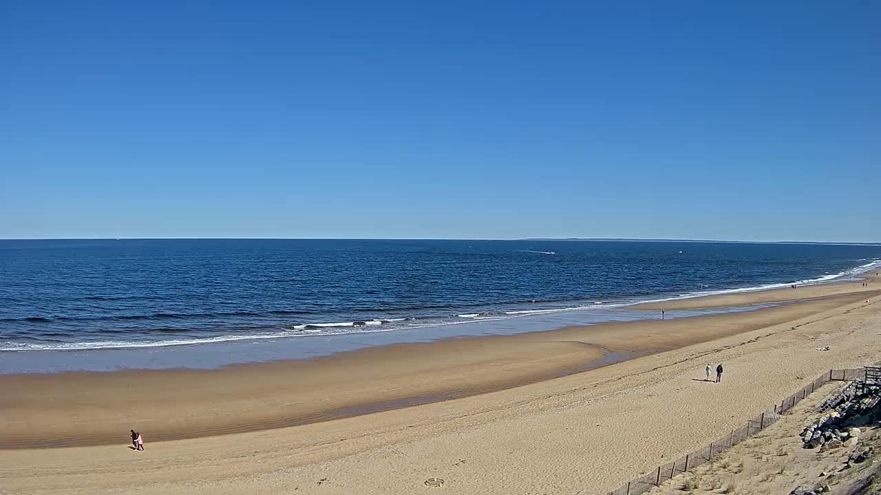 A long, sandy beach stretches along a calm, blue ocean under a clear, sunny sky.