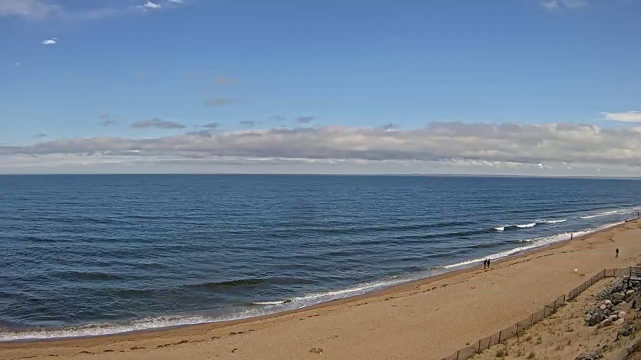 A sandy beach curves gently into a calm, blue ocean under a partly cloudy sky.