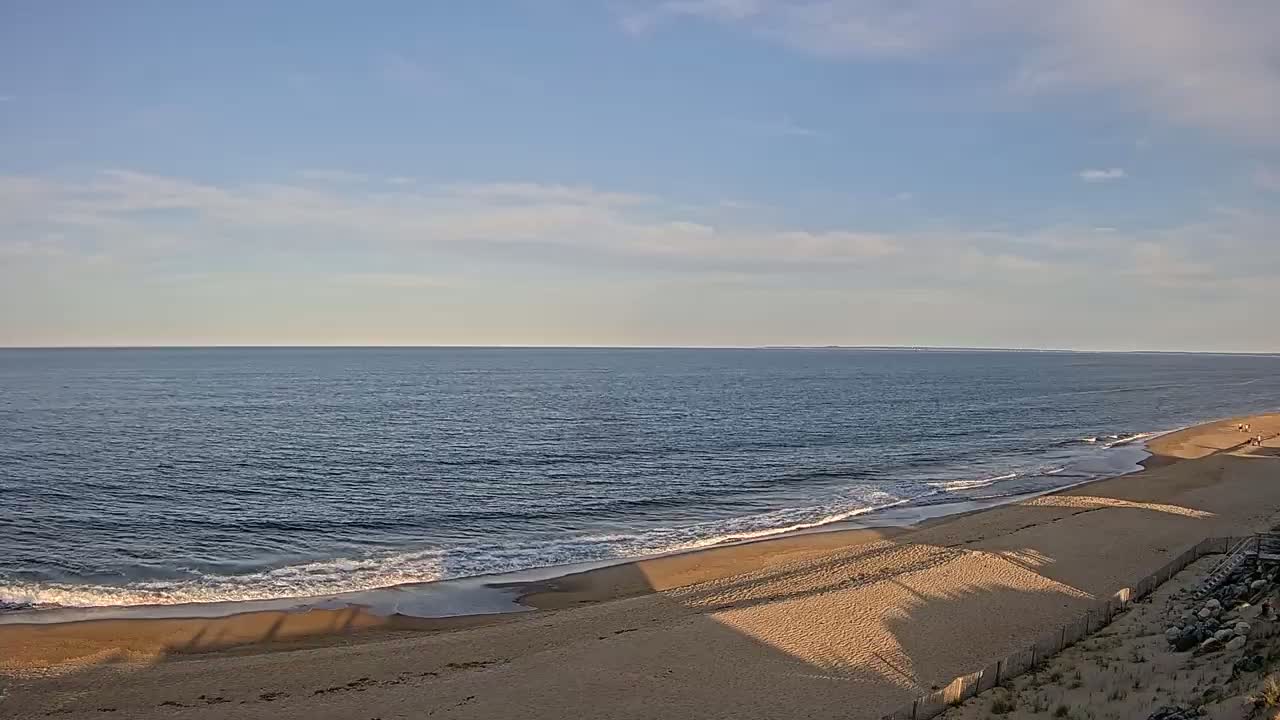 A wide sandy beach slopes down to a calm ocean under a mostly clear sky.