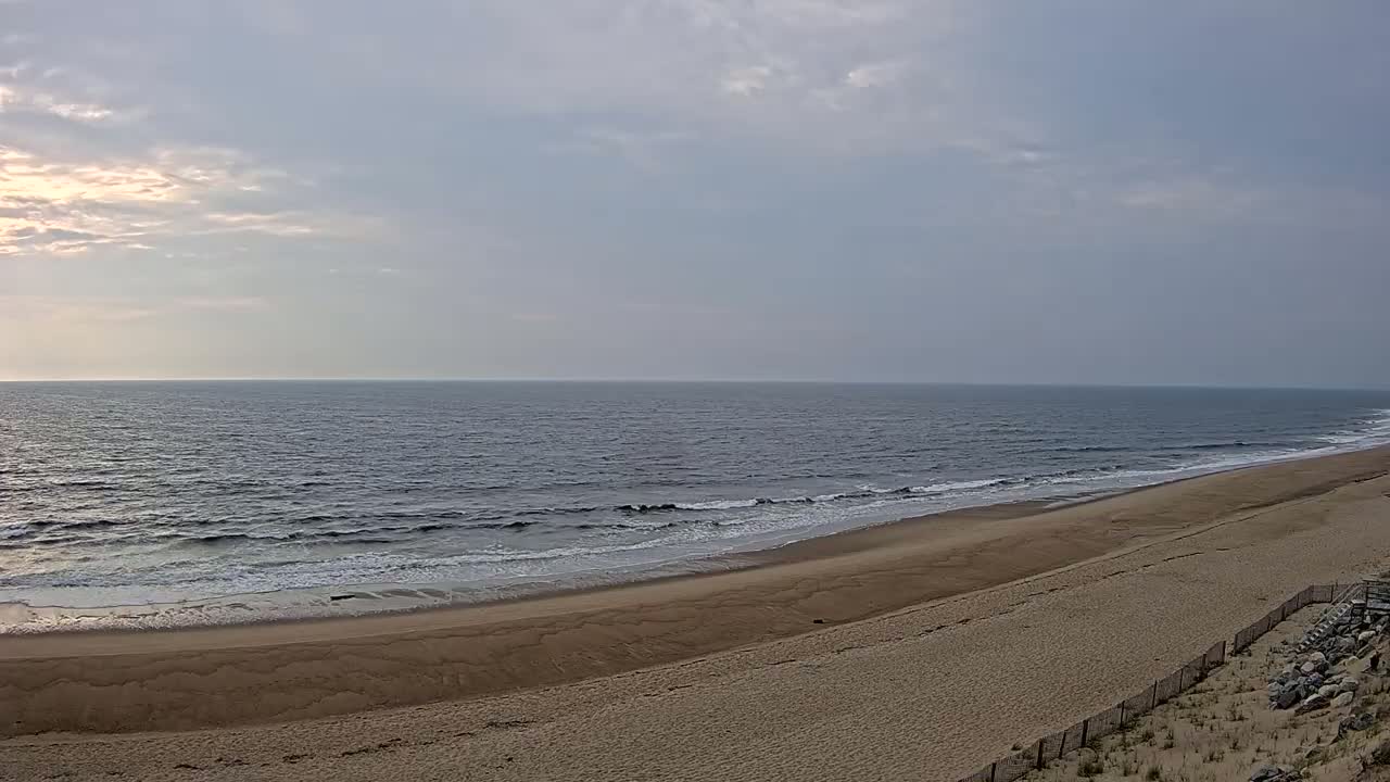 A wide sandy beach slopes gently down to a calm ocean under a mostly cloudy sky.