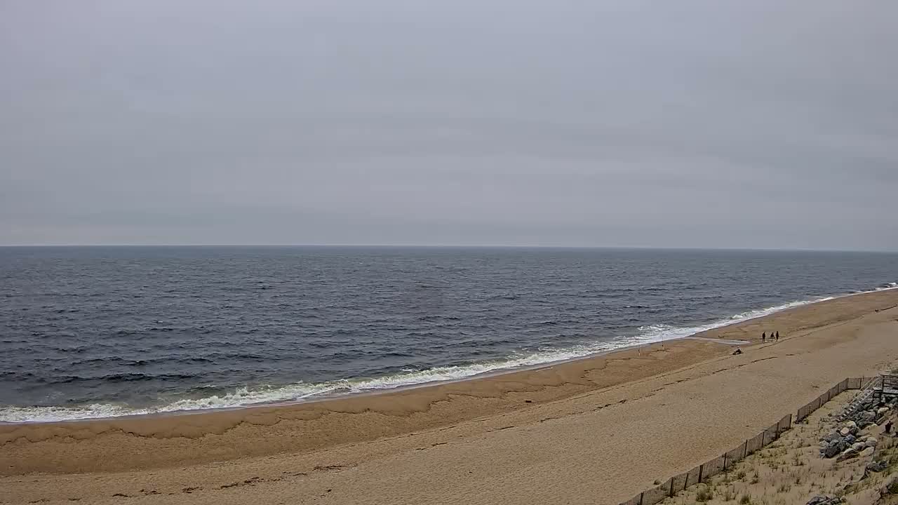 A long, sandy beach slopes down to a dark, wavy ocean under an overcast sky.