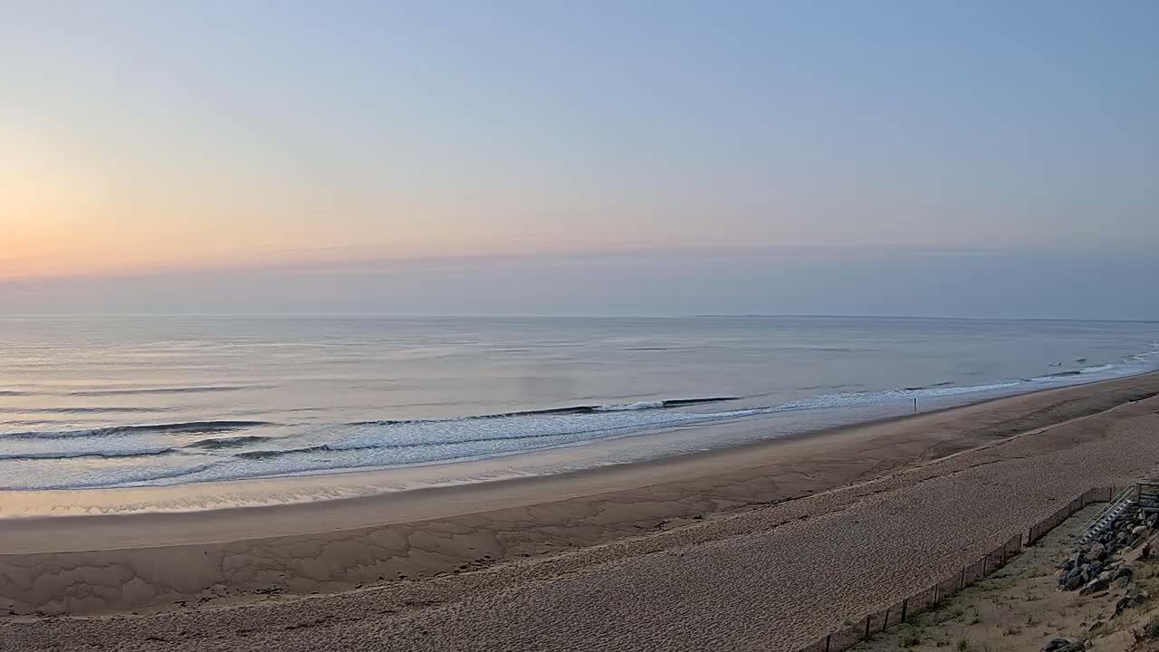 A sandy beach slopes down to a calm ocean under a pale sunrise.