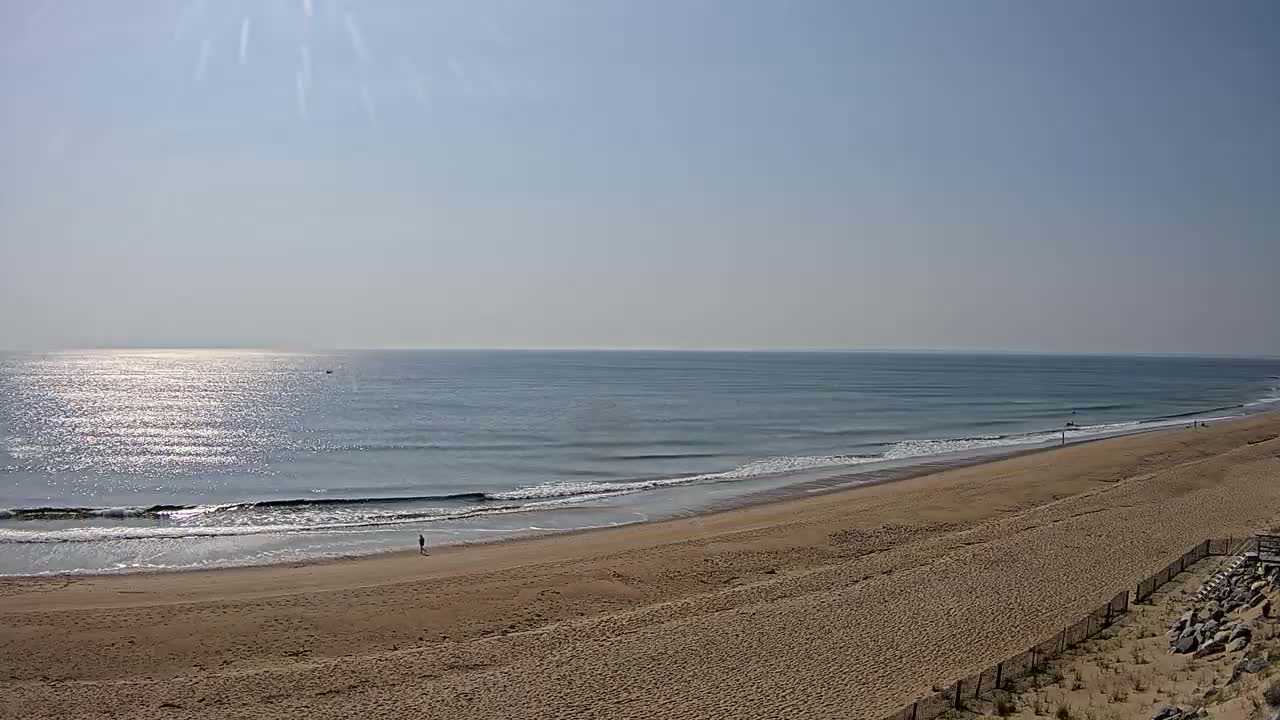 A sandy beach slopes down to a calm, sunlit ocean with a few small waves under a clear sky.