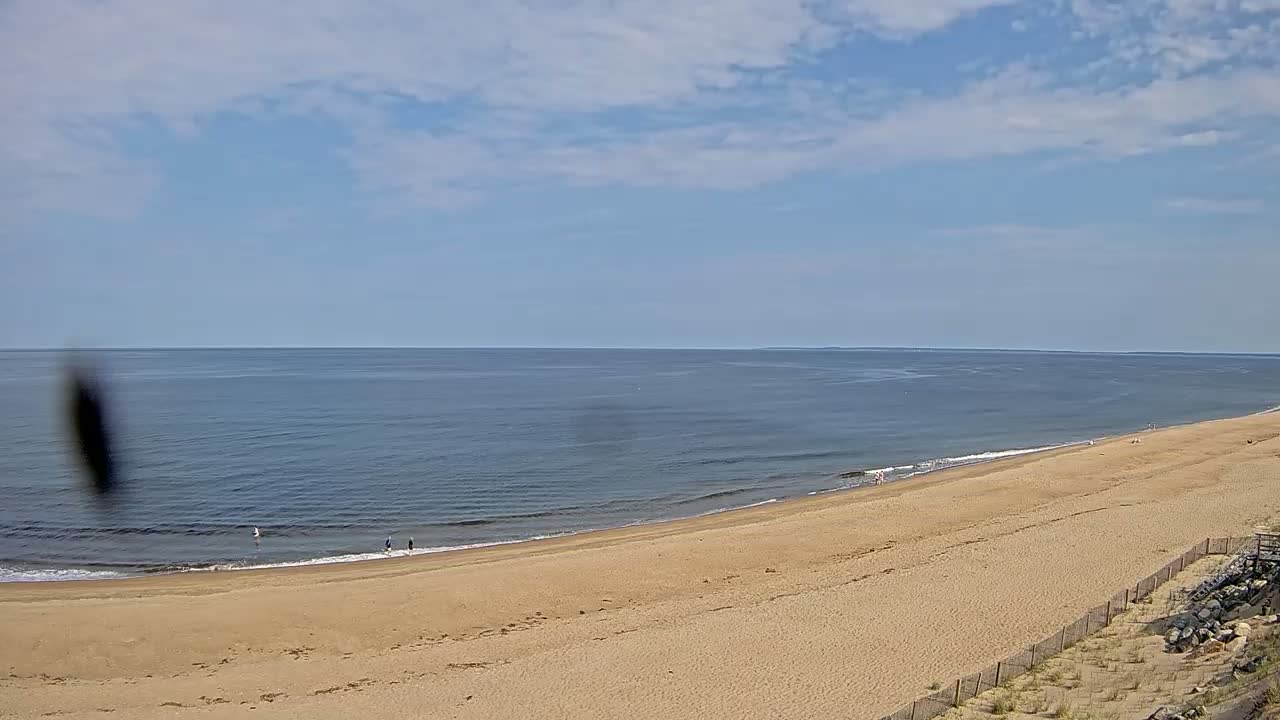 A long sandy beach slopes down to a calm ocean under a partly cloudy sky.