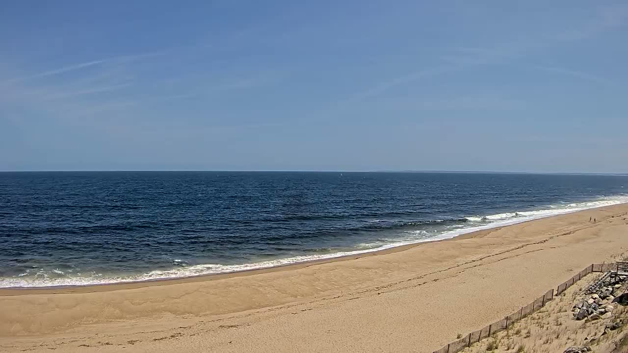 A sandy beach curves gently alongside a dark blue ocean under a clear, bright sky.
