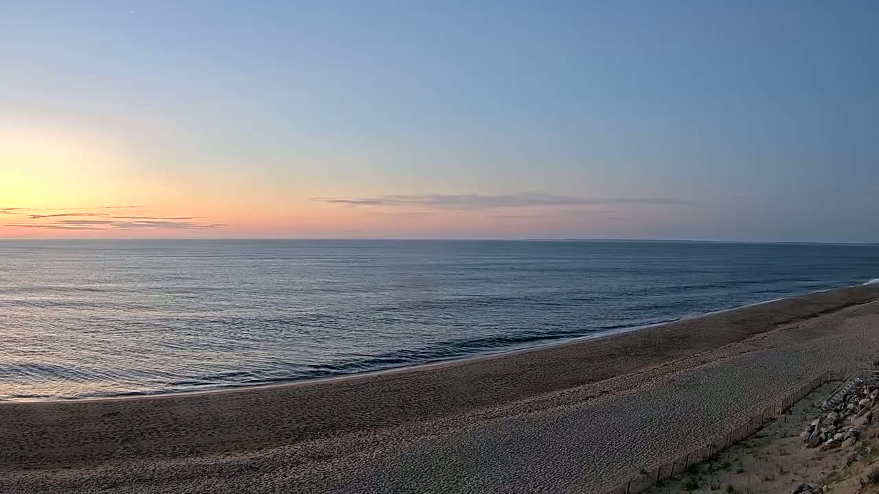 A sandy beach slopes down to a calm ocean under a pale sunrise sky.