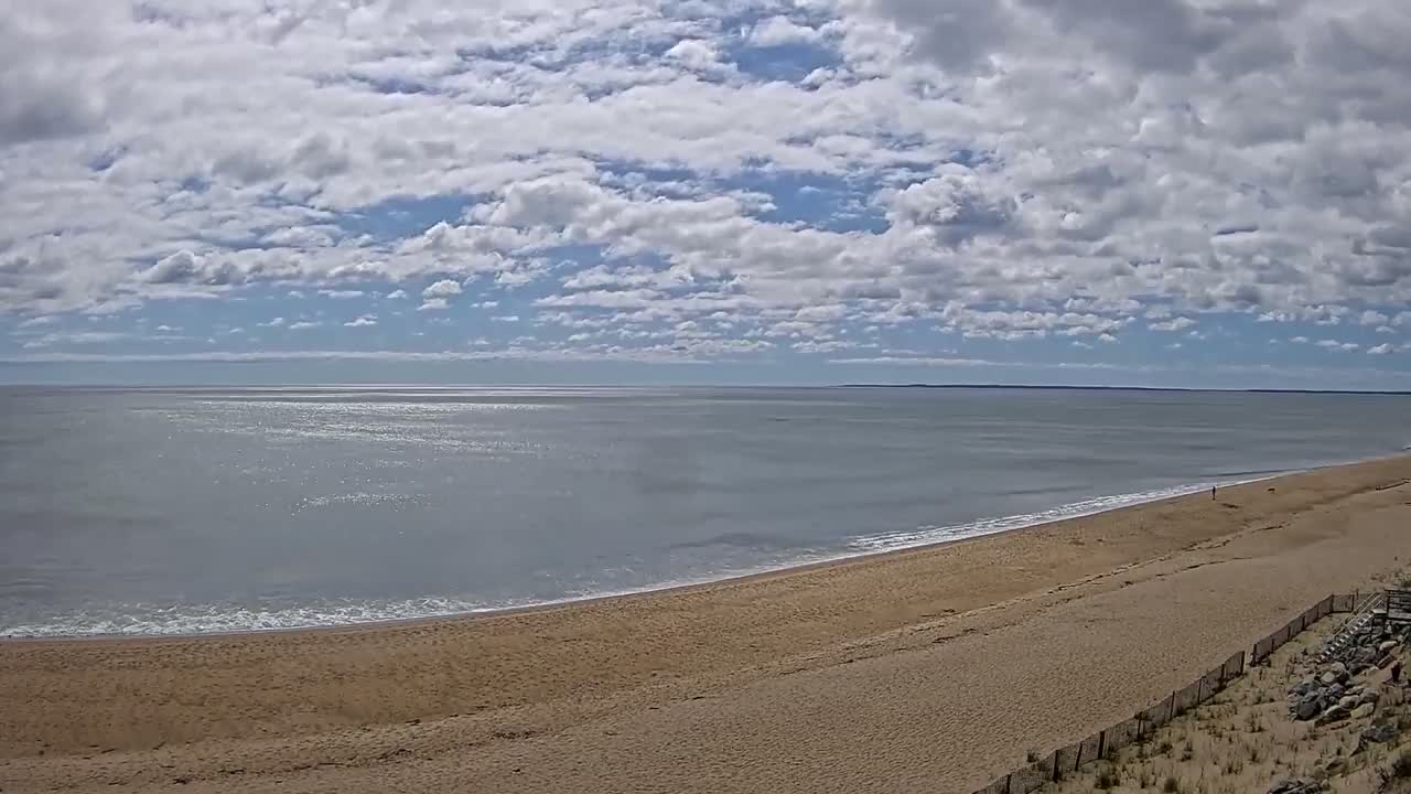 A sandy beach curves gently into a calm ocean under a partly cloudy sky.