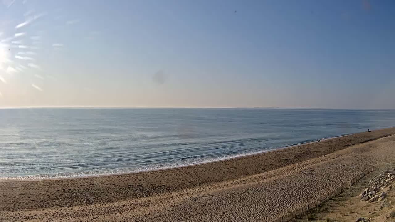 A sandy beach slopes down to a calm ocean under a clear, sunny sky.