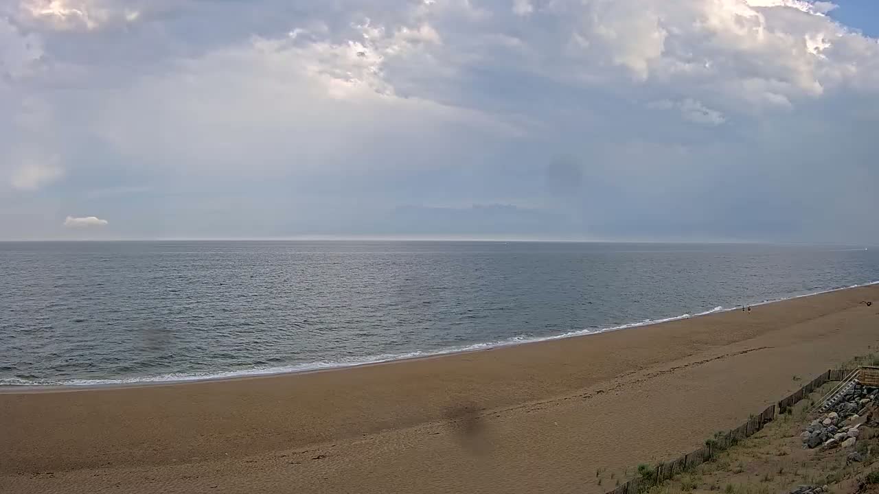 A wide sandy beach slopes gently to a calm ocean under a partly cloudy sky.