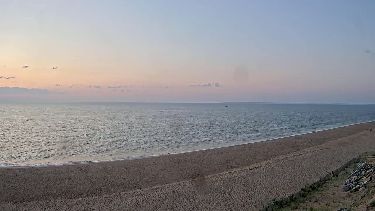 A wide sandy beach slopes gently to a calm ocean under a partly cloudy sky.