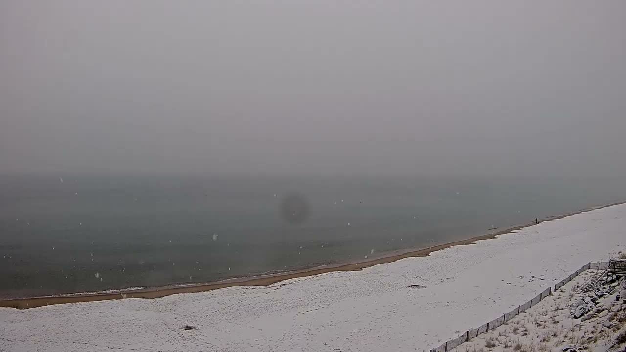 A wide sandy beach slopes gently to a calm ocean under a partly cloudy sky.
