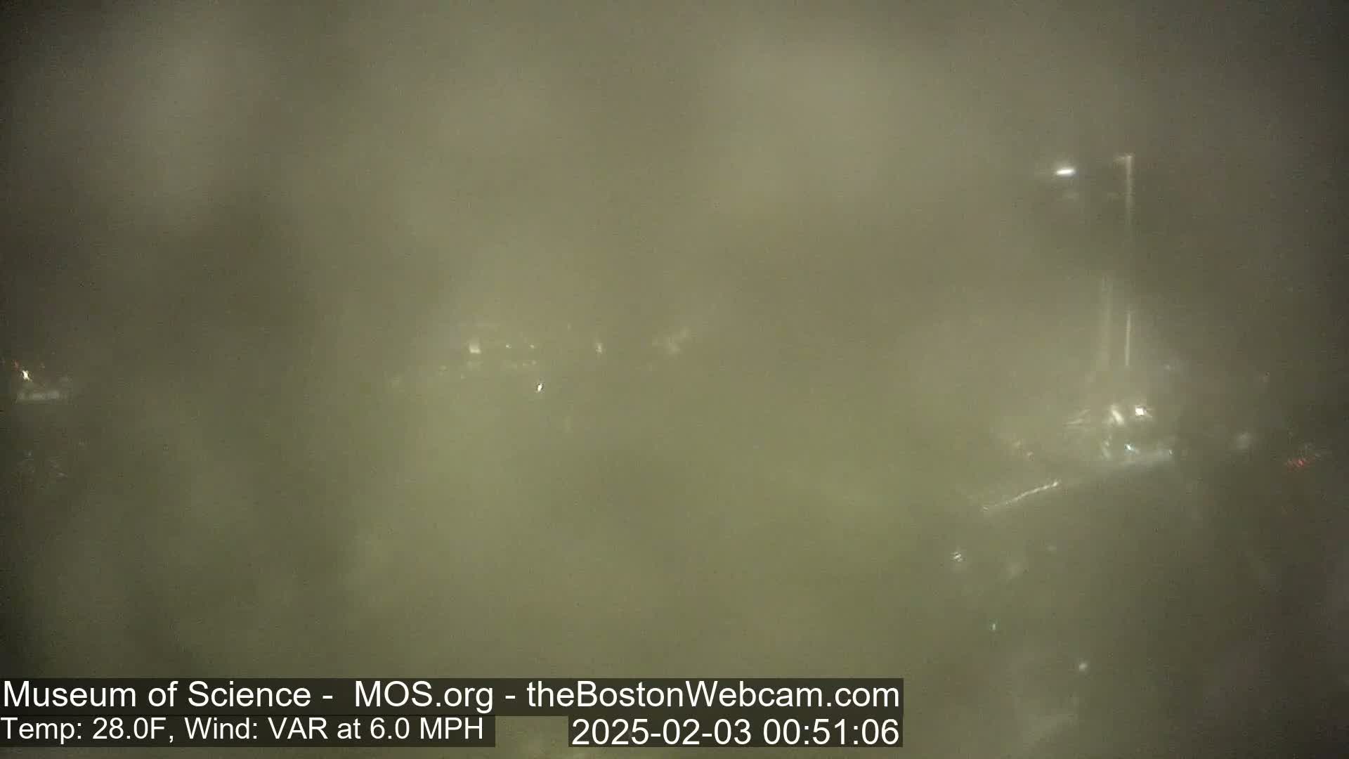 A foggy nighttime scene shows indistinct shapes of buildings and a tall light post.