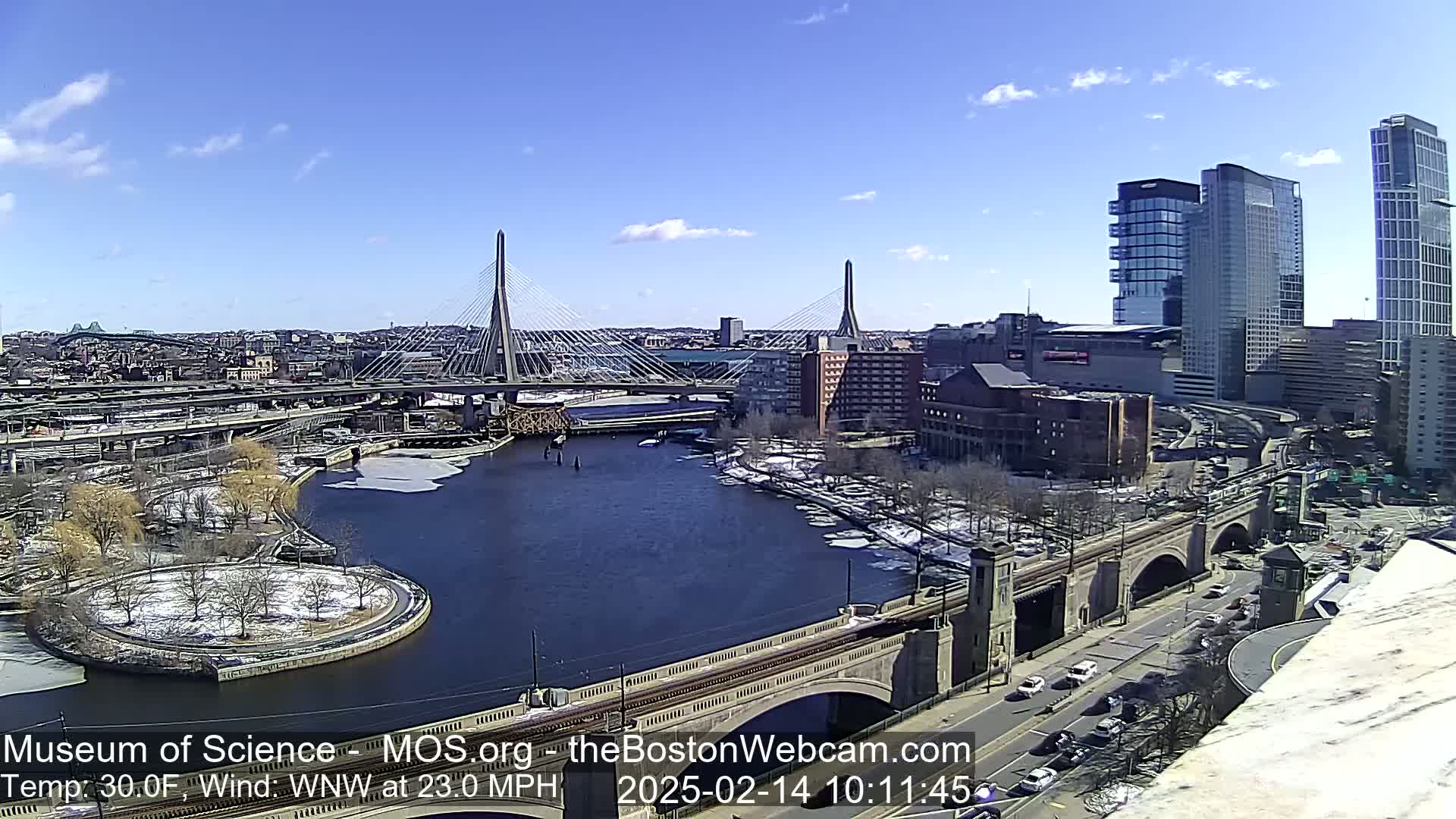A sunny day with a 23 mph wind shows a cityscape with a river, bridges, and modern and older buildings.