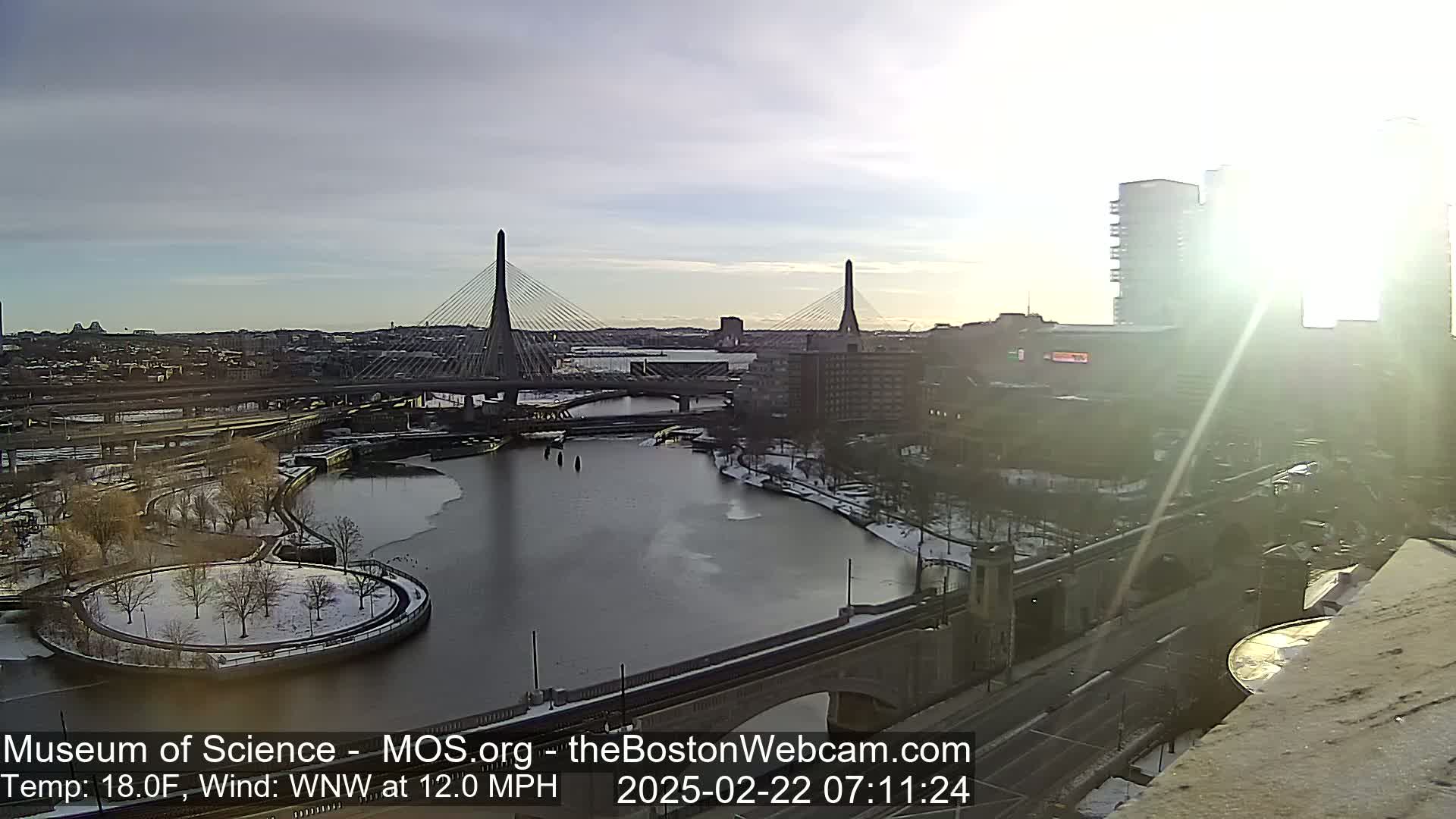 A partly sunny, cold day with a strong wind shows a partly frozen river, two cable-stayed bridges, and a cityscape with snow-covered ground.