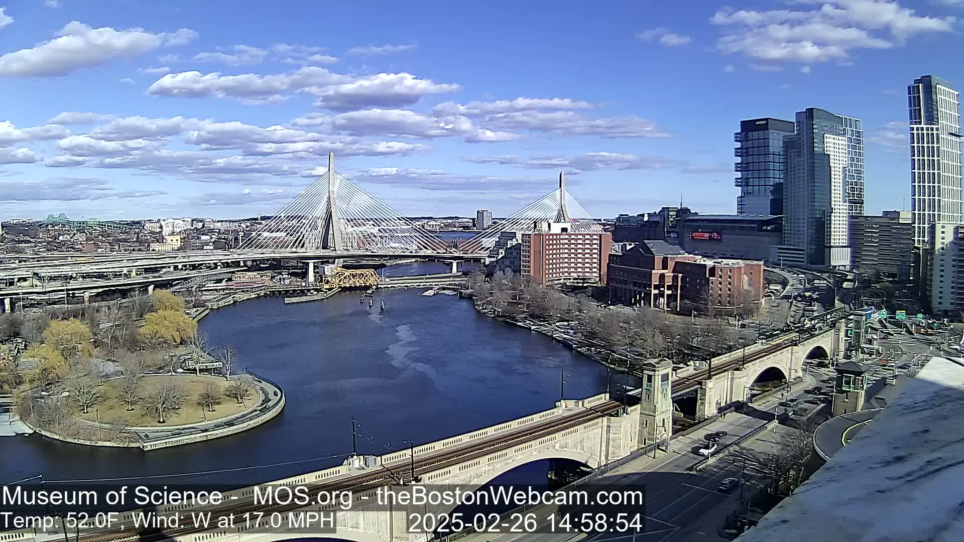 A sunny day with a 17 mph westerly wind shows a cityscape with two cable-stayed bridges spanning a river, alongside other bridges and buildings.