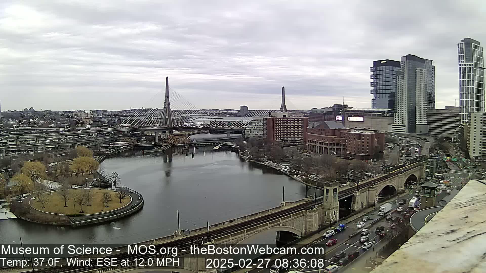 A cityscape with two cable-stayed bridges spanning a river under an overcast sky.