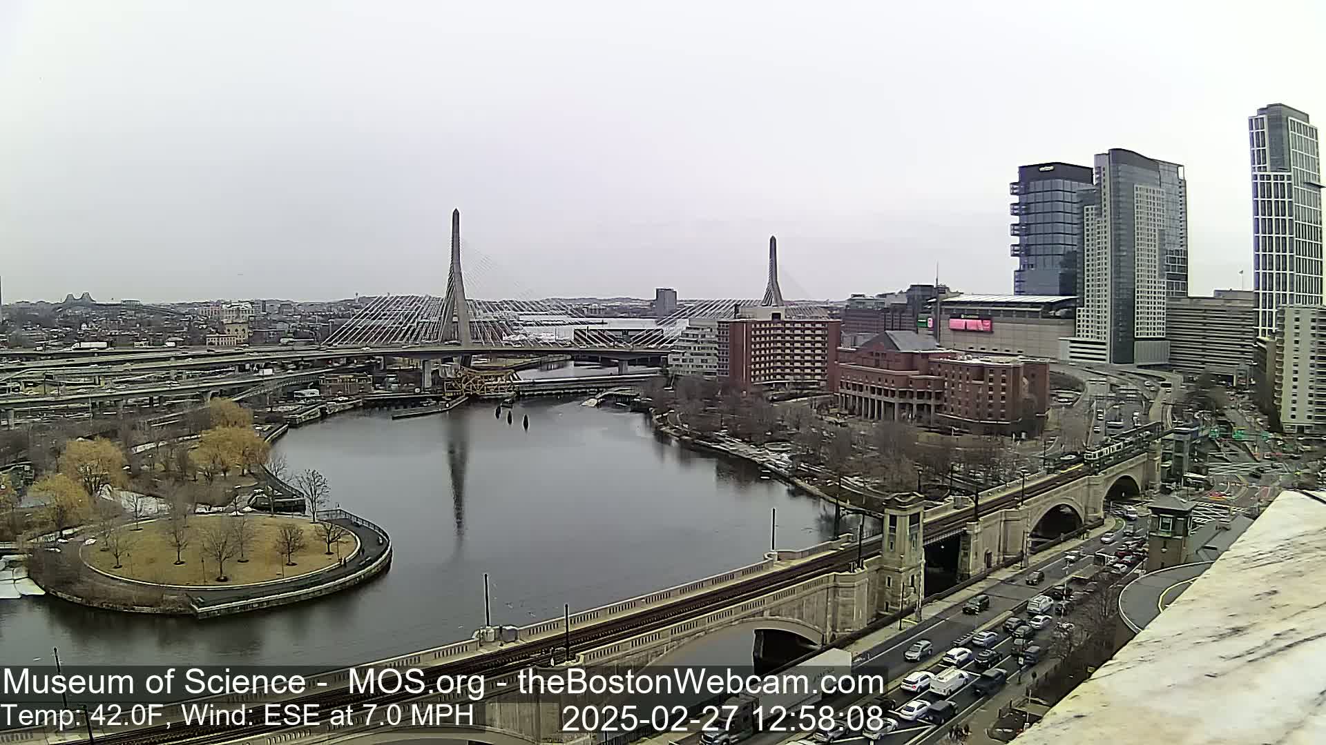 A cityscape featuring two cable-stayed bridges over a river, with overcast skies and a temperature of 42 degrees Fahrenheit.