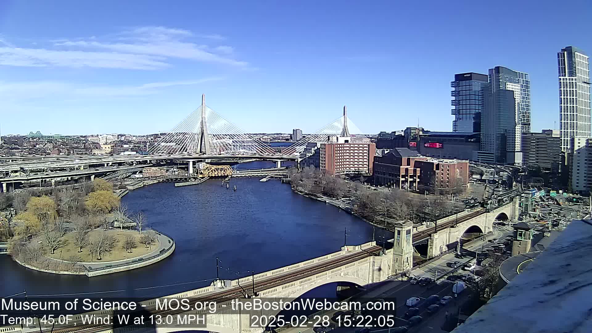 A sunny day shows a city skyline with two cable-stayed bridges spanning a river, alongside a smaller stone arch bridge and other roadways.