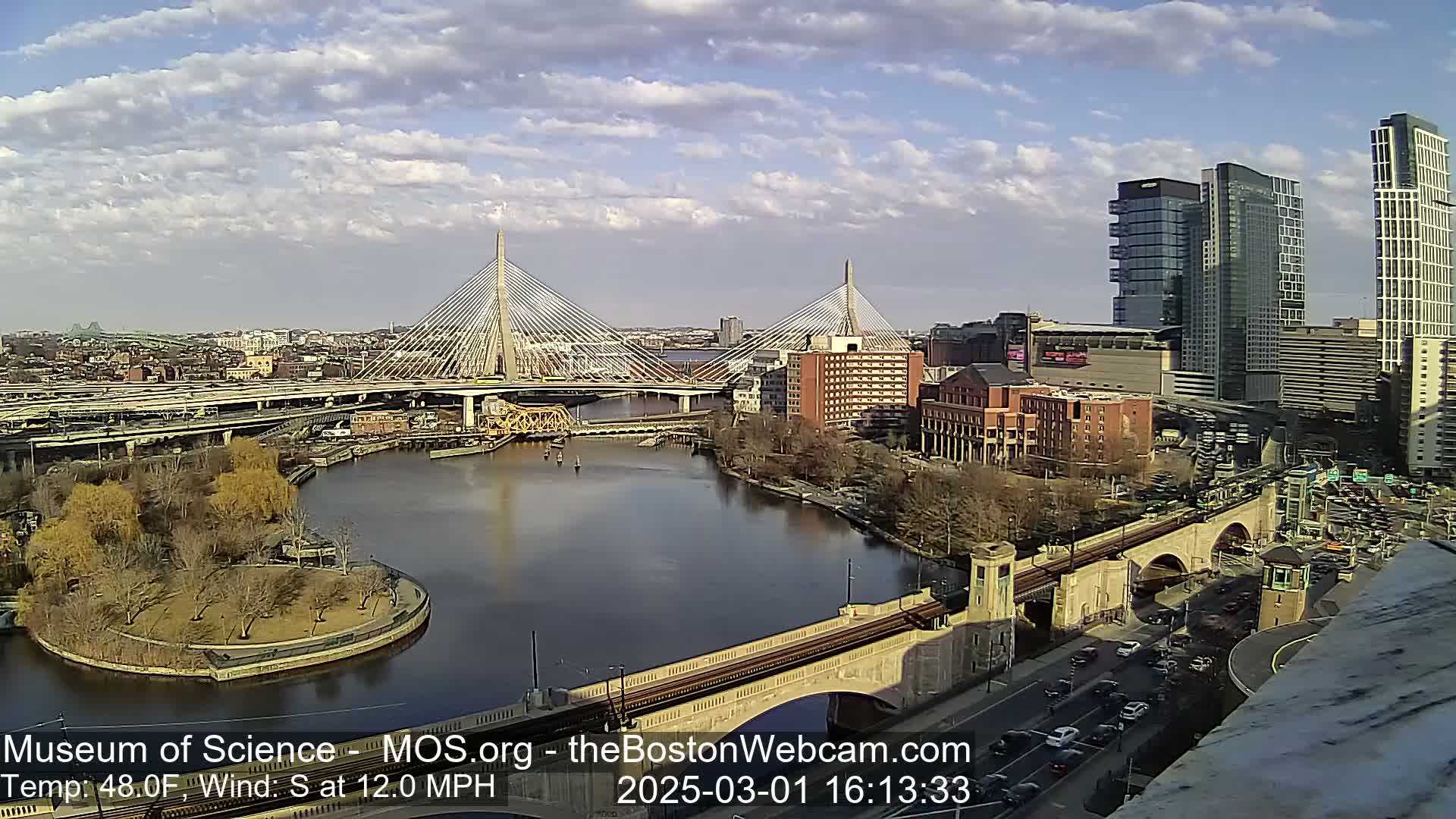 A partly cloudy day with a south wind at 12 mph shows a cityscape with two cable-stayed bridges spanning a river, along with other bridges and city buildings.